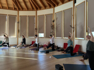 Women practicing side-stretch yoga poses inside a circular cedar studio at the Sentinel Yoga & Journaling Retreat in Kaslo, British Columbia, 2023.