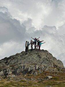Group of women celebrating on a rocky summit in the Monashee Mountains during the 2025 Revelstoke Retreat, arms raised against a dramatic cloudy sky.