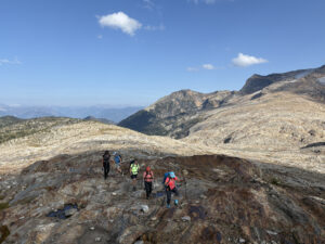 Group of women hiking across alpine terrain in the Monashee Mountains during a 2025 Revelstoke hiking and yoga retreat, west of Revelstoke, BC, with panoramic views of rocky ridgelines and distant peaks.