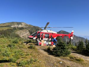 Helicopter with 4 people and a bunch of stuff in front of it with mountains in the background