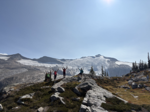 A group of four hiking with poles up posing in front of blanket glacier