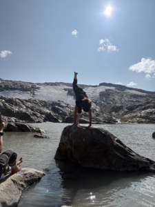 woman doing a yoga pose in front of a glacier on a rock in a lake
