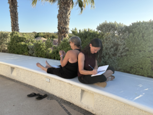 Two women sitting back to back sketching.