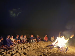 A group of people sitting around a fire on the beach